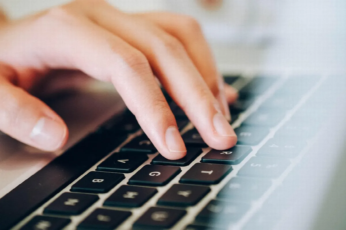 Mãos digitando em laptop sobre mesa de trabalho